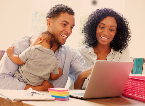 Family looking at laptop holding baby A women, and a man holding a baby working on a laptop